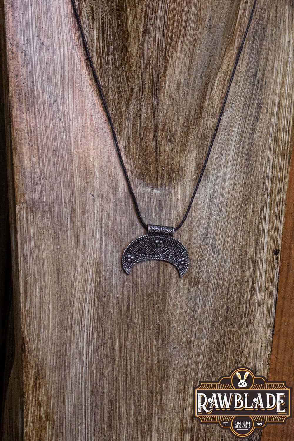 Rawblade's Western Lunula pendant in silver on an adjustable cord, displayed on wooden background.