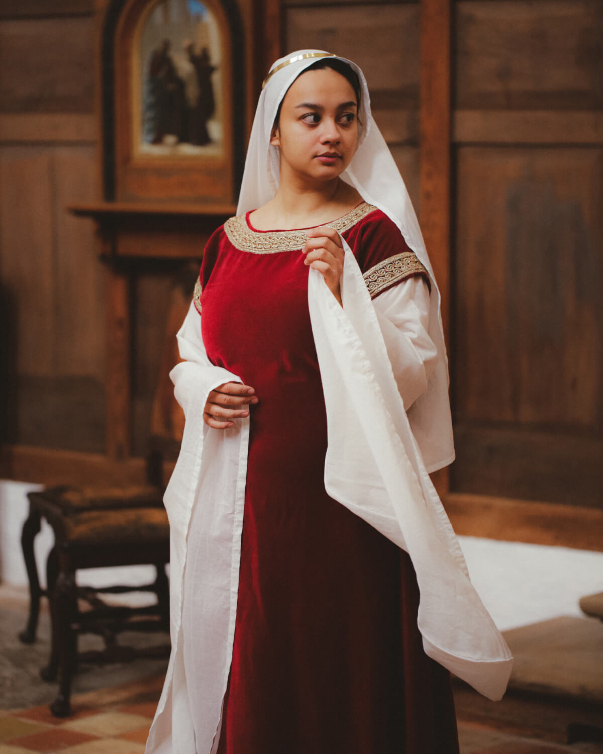 Woman modeling Bliaut Noble dress with oval veil in medieval setting