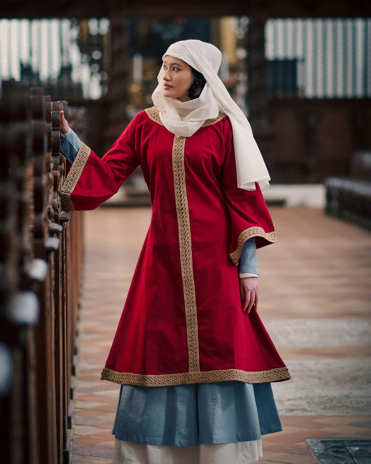 Woman wearing red medieval over tunic with white wimple in a church
