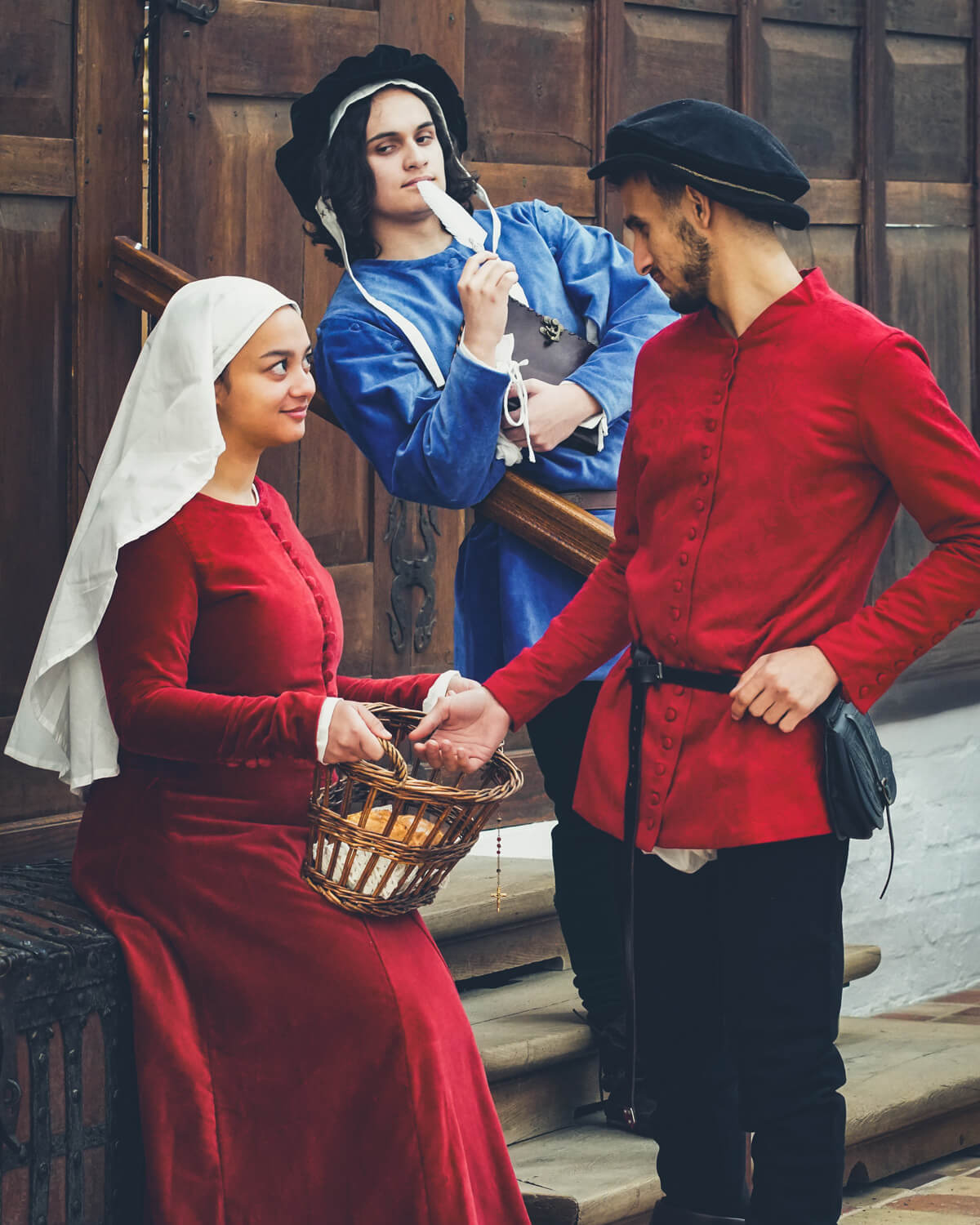 Medieval man and woman in red, man in blue costume in background.