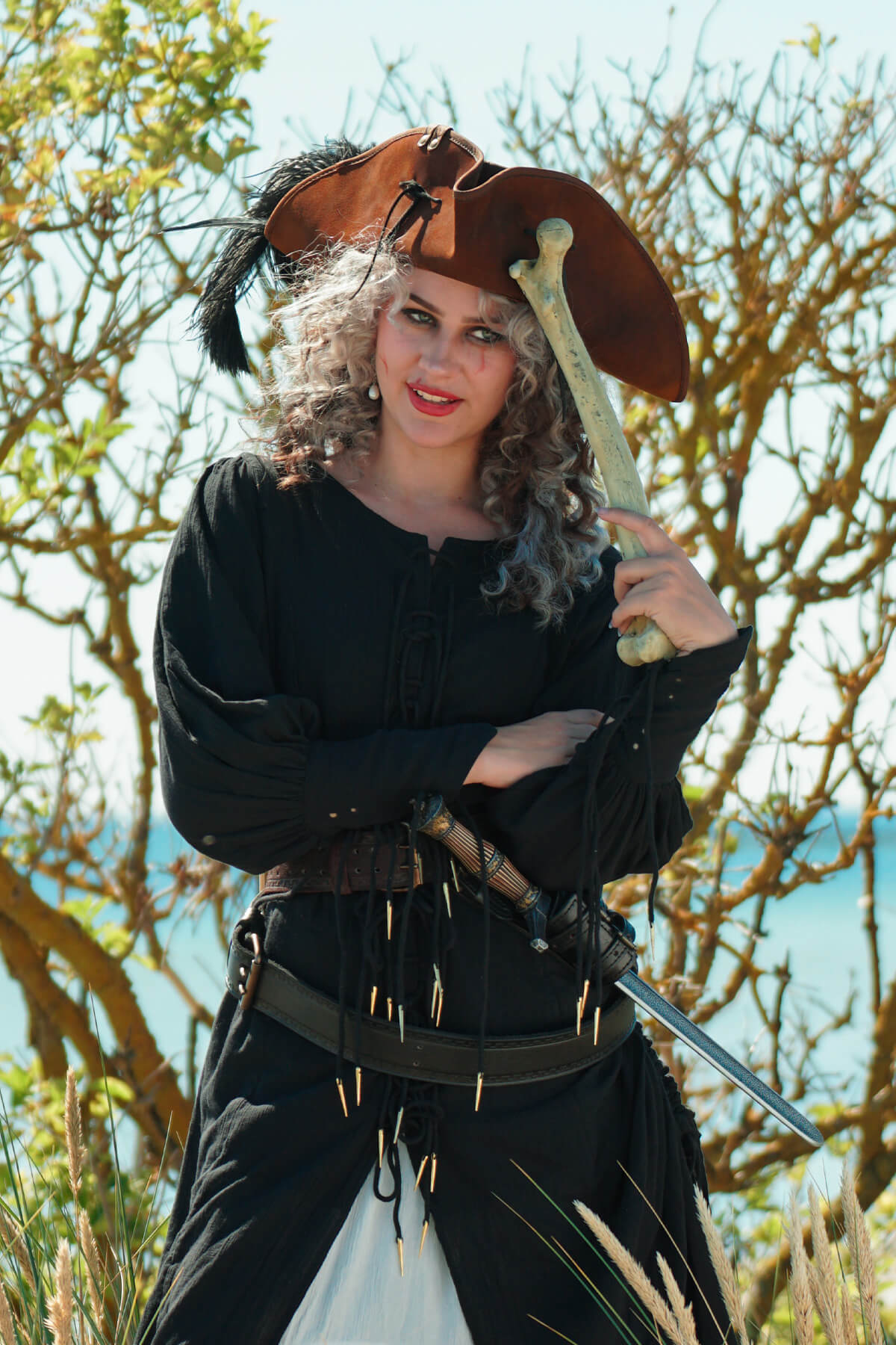 Person in pirate costume holding a sword with trees and sky in the background