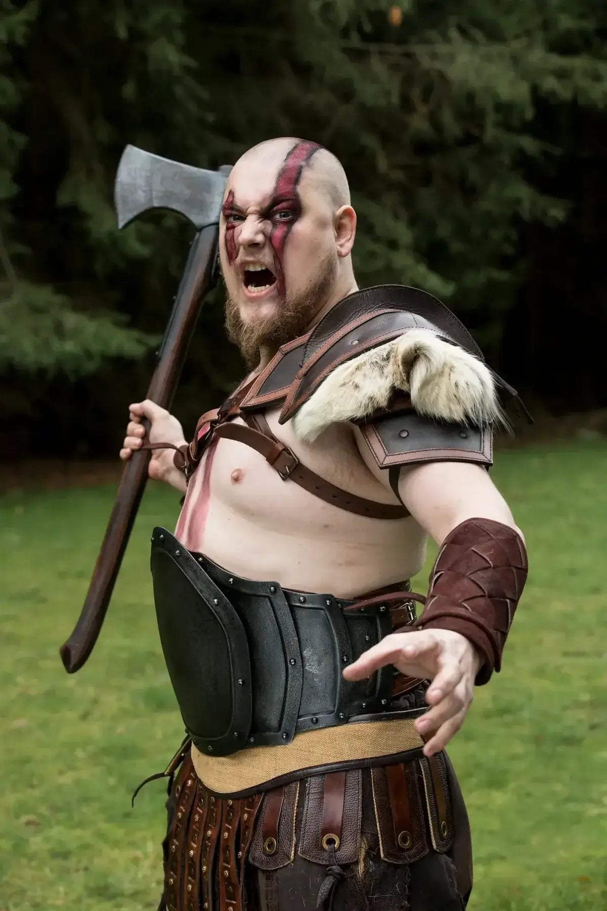 Person dressed as a warrior with an axe, wearing armor and fur, outdoors.