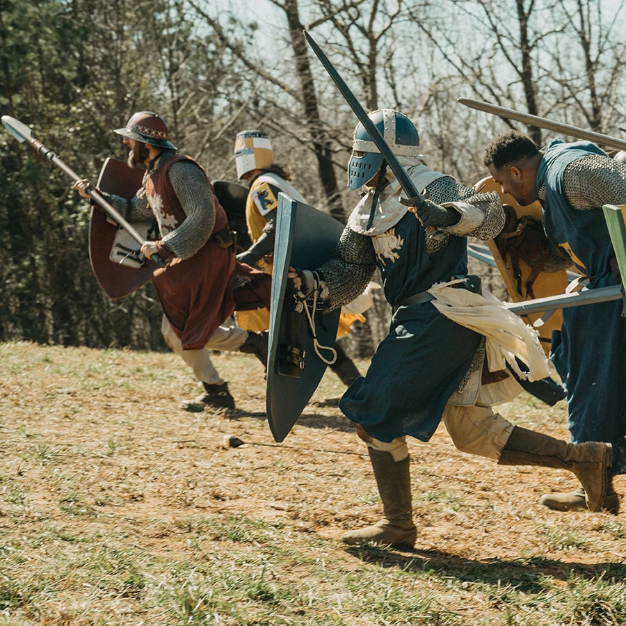 Medieval LARP warriors in armor with shields and spears running across a field.