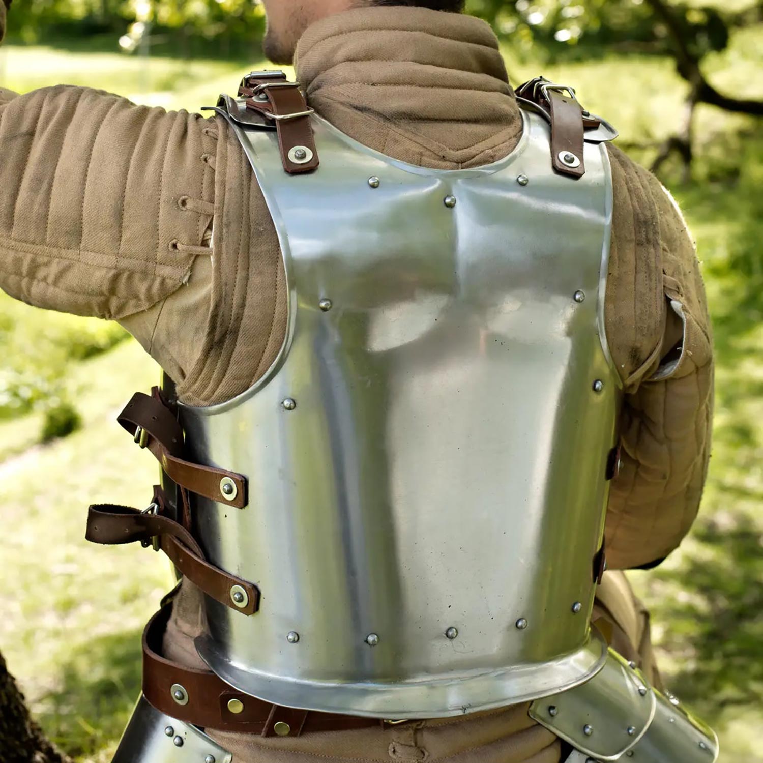 Person wearing a metal backplate outdoors with greenery in the background
