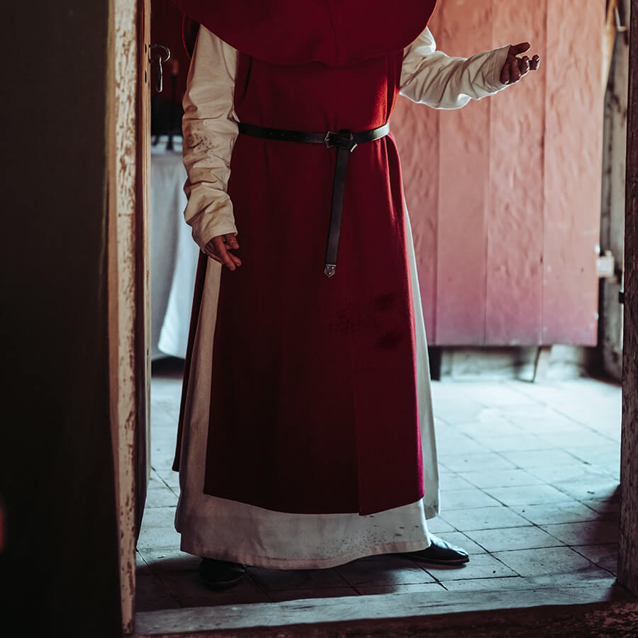 Person wearing a red robe and white shirt standing in a doorway.